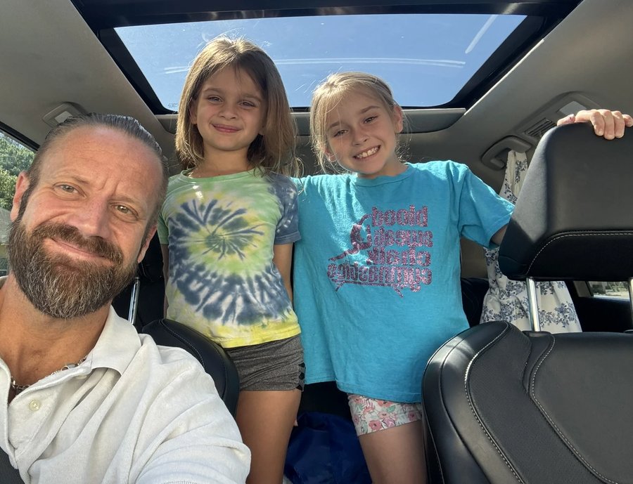 A father taking a selfie with his two daughters in the car