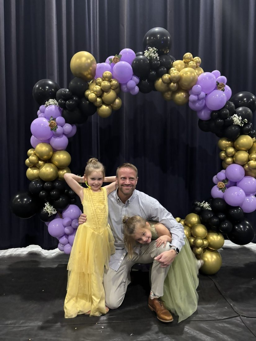 A father with his two daughters under a balloon arch